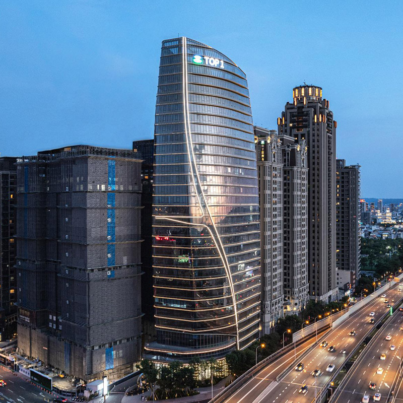 Aedas’ Taichung TOP 1 National Financial Center is shown as a sculptural high‑rise office tower with a smooth, S‑curved glass façade inspired by the flowing lines of a traditional qipao. The image highlights a luminous vertical profile accented by horizontal lighting bands and a refined podium, forming a prominent financial landmark that integrates modern corporate identity with cultural symbolism along Taichung’s urban skyline.