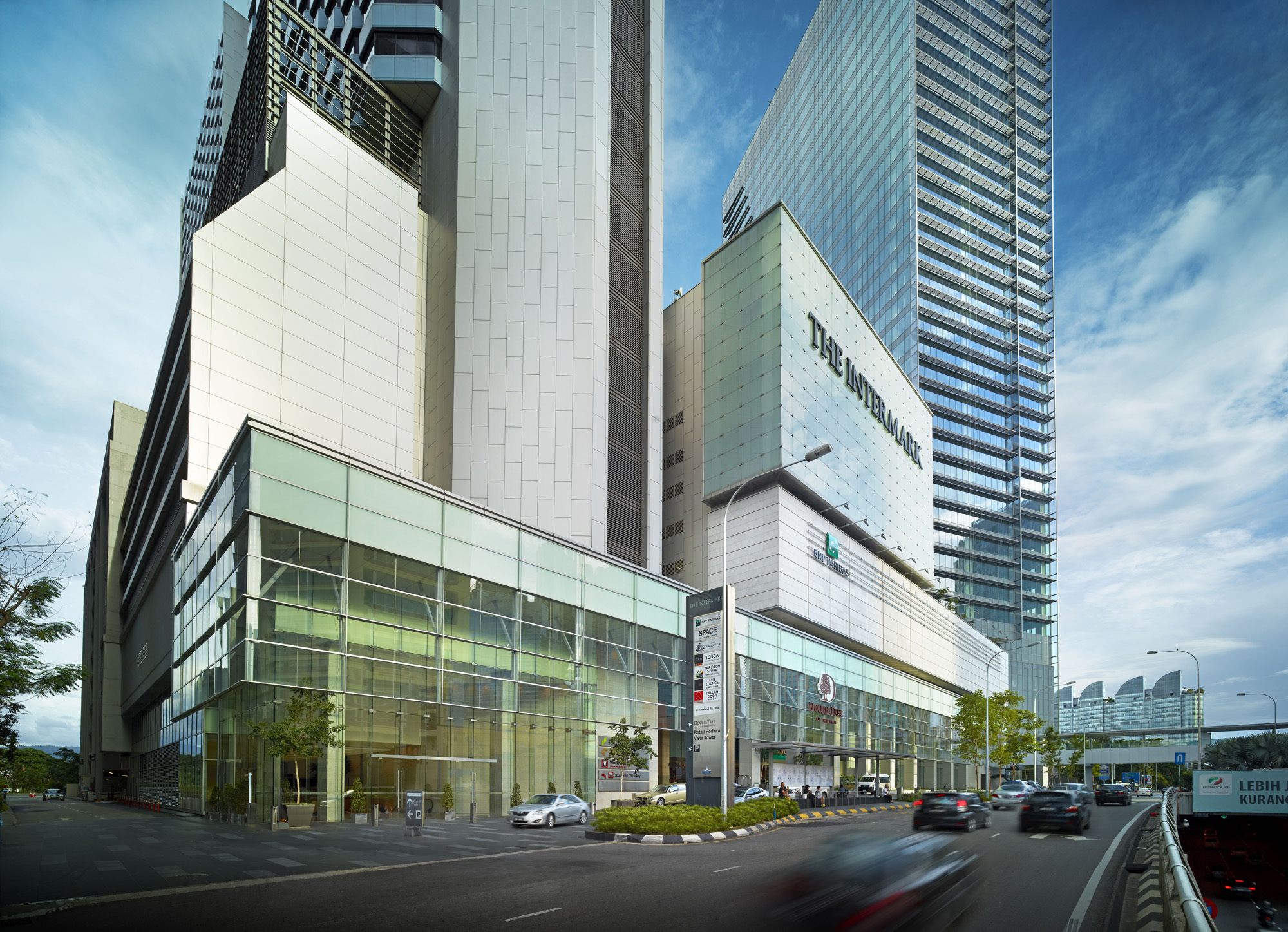 Aedas’ The Intermark in Kuala Lumpur is shown as a prominent mixed‑use podium with expansive curtain‑wall glazing, clearly articulated retail frontages, and upper towers rising above. The image highlights a refreshed urban complex combining office, hotel, and retail functions, where transparent façades, active street edges, and contemporary massing create a cohesive commercial and hospitality destination within the city core.