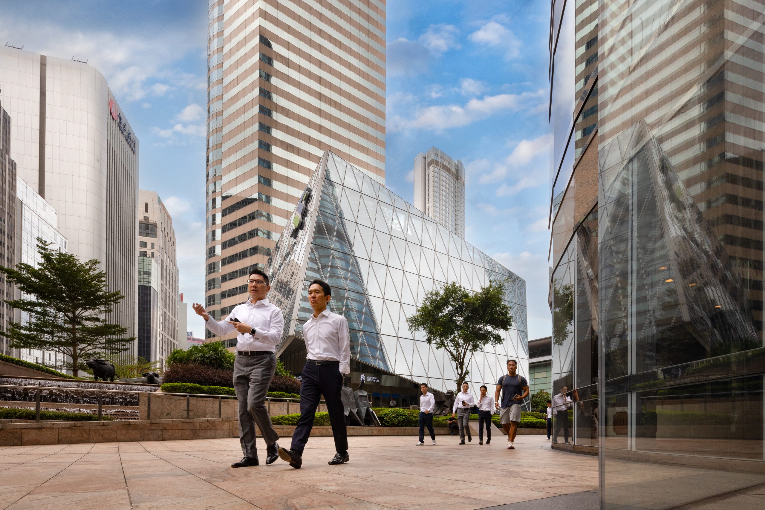 Aedas’ The Forum with faceted glass pavilion, open plaza and column‑free Grade‑A office interior. Ground‑level view of Aedas‑designed The Forum at Exchange Square, showing a faceted, gem‑like glass pavilion opening onto an urban plaza in Central Hong Kong. The building features a double‑height glazed lobby, inclined glass façade planes and covered pedestrian walkways, framed by surrounding commercial towers and landscaped public space.