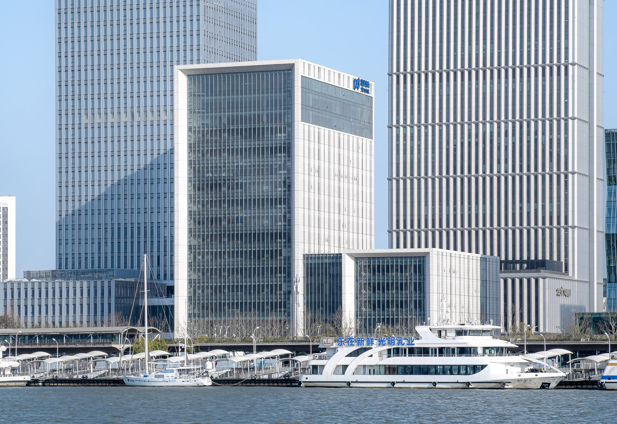 Aedas’s Shanghai Pudong Development Bank new office is shown as a mid‑ to high‑rise commercial building with a rectilinear tower form, high‑performance glazed curtain wall, and articulated podium volumes along a waterfront edge. The image highlights contemporary office architecture integrated into Shanghai’s dense financial district skyline.