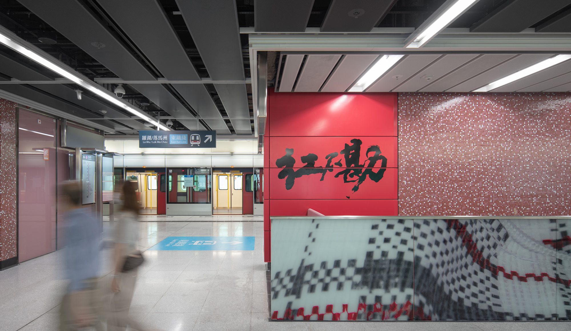 Aedas’s Hung Hom Station on the MTR Tuen Ma Line is shown with a linear platform‑adjacent concourse, exposed modular ceiling panels, integrated lighting, full‑height platform screen doors, and graphic wall finishes identifying the station. The image highlights contemporary metro architecture focused on clarity, robustness, and passenger circulation in Hong Kong.
