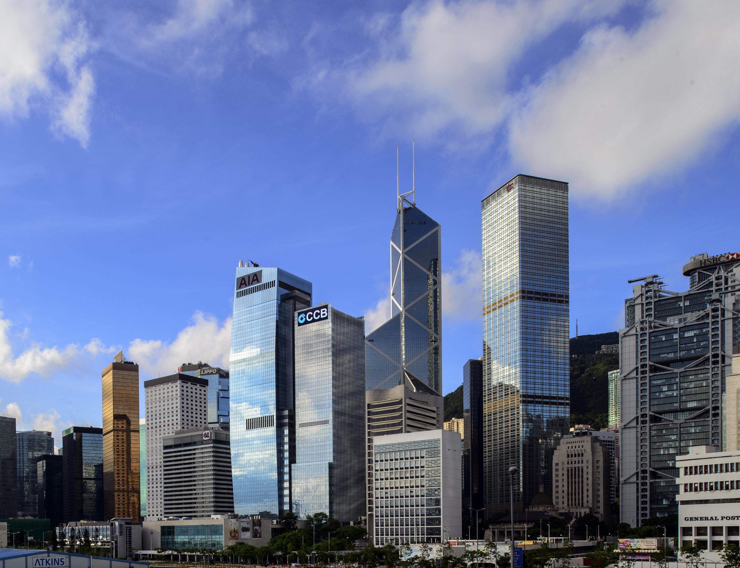 Aedas’ China Construction Bank Tower in Hong Kong is shown as a sleek Grade‑A office tower along the Central waterfront, characterised by a disciplined vertical glass façade with strong linear articulation and stepped massing. The image highlights a refined corporate landmark framed by Victoria Harbour and mountain backdrops, conveying institutional authority, elegance, and clarity within Hong Kong’s dense financial skyline.