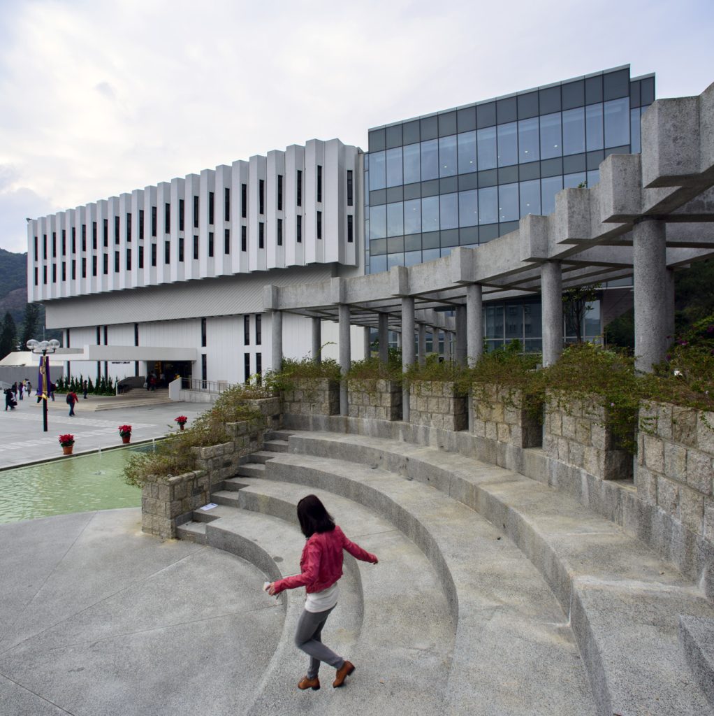 Aedas’s Chinese University of Hong Kong Library Extension is shown as an elevated institutional building combining a finned concrete façade, a transparent glazed volume, and a colonnaded plinth. The image highlights campus‑integrated architecture with layered massing, structural clarity, and stepped public terraces within a sloped hillside setting.