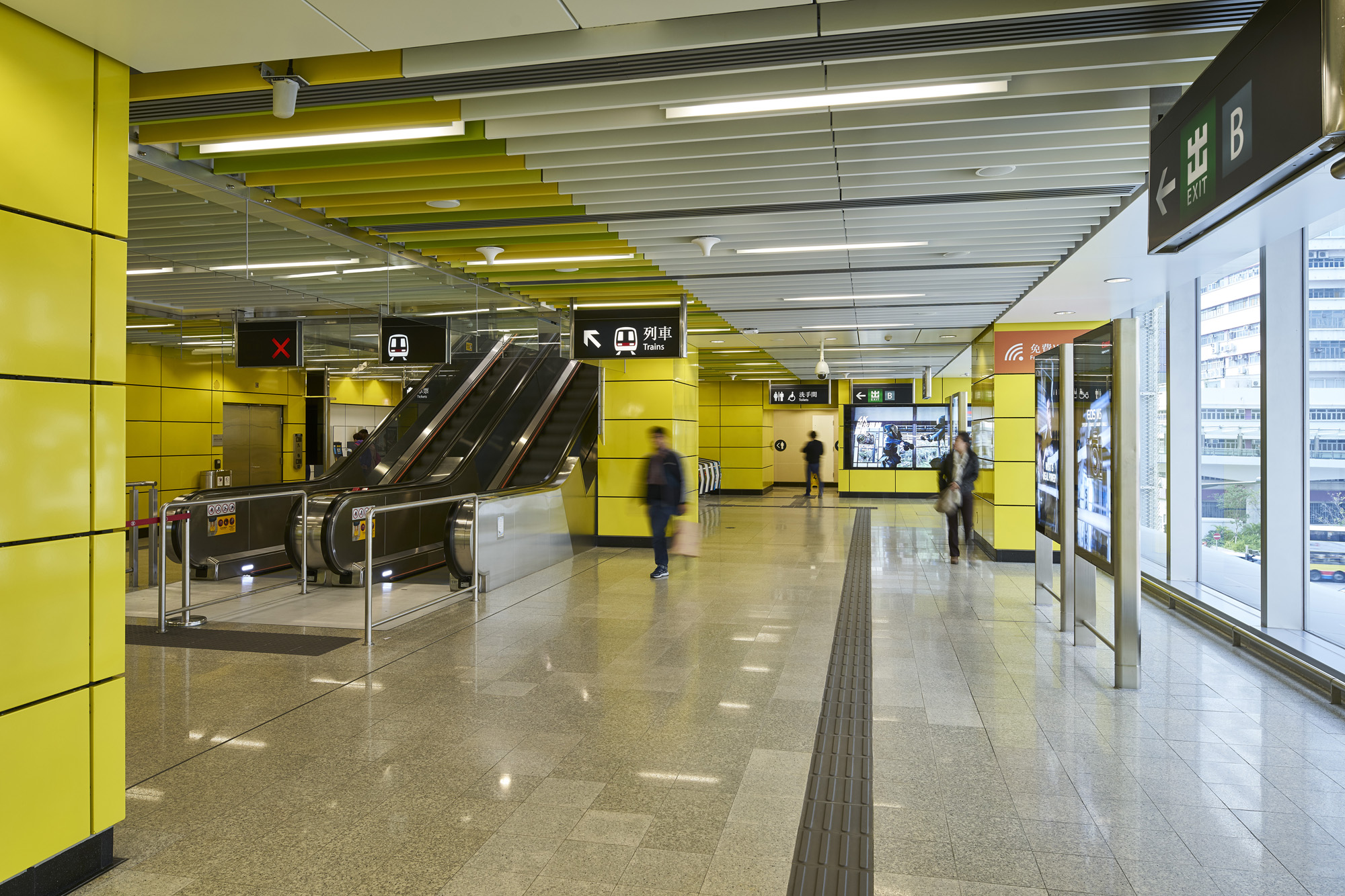 Aedas’s Wong Chuk Hang Station on the MTR South Island Line is shown with a wide concourse space, linear ceiling panel system, integrated lighting, escalator banks, and continuous wall finishes. The image highlights contemporary metro architecture designed for clear passenger movement, spatial legibility, and robust station infrastructure in Hong Kong.