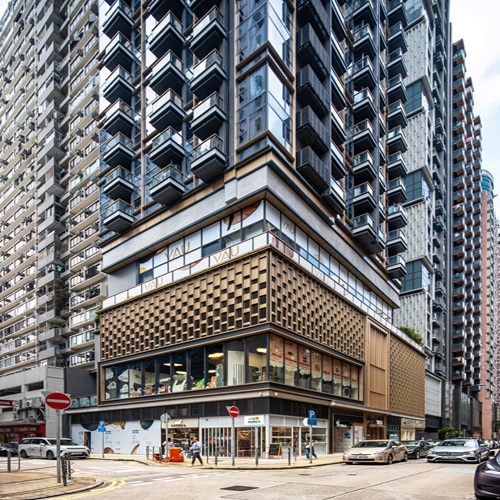 Aedas’ VAU Residence in Hong Kong is shown as a contemporary residential tower with a finely articulated podium clad in perforated champagne‑gold aluminium panels and full‑height glazing at street level. The image highlights stacked balconies with glass balustrades, light grey curtain‑wall façades, and metal accents that create rich light‑and‑shadow effects, establishing a refined Southern European‑inspired landmark within the dense Ho Man Tin urban streetscape.