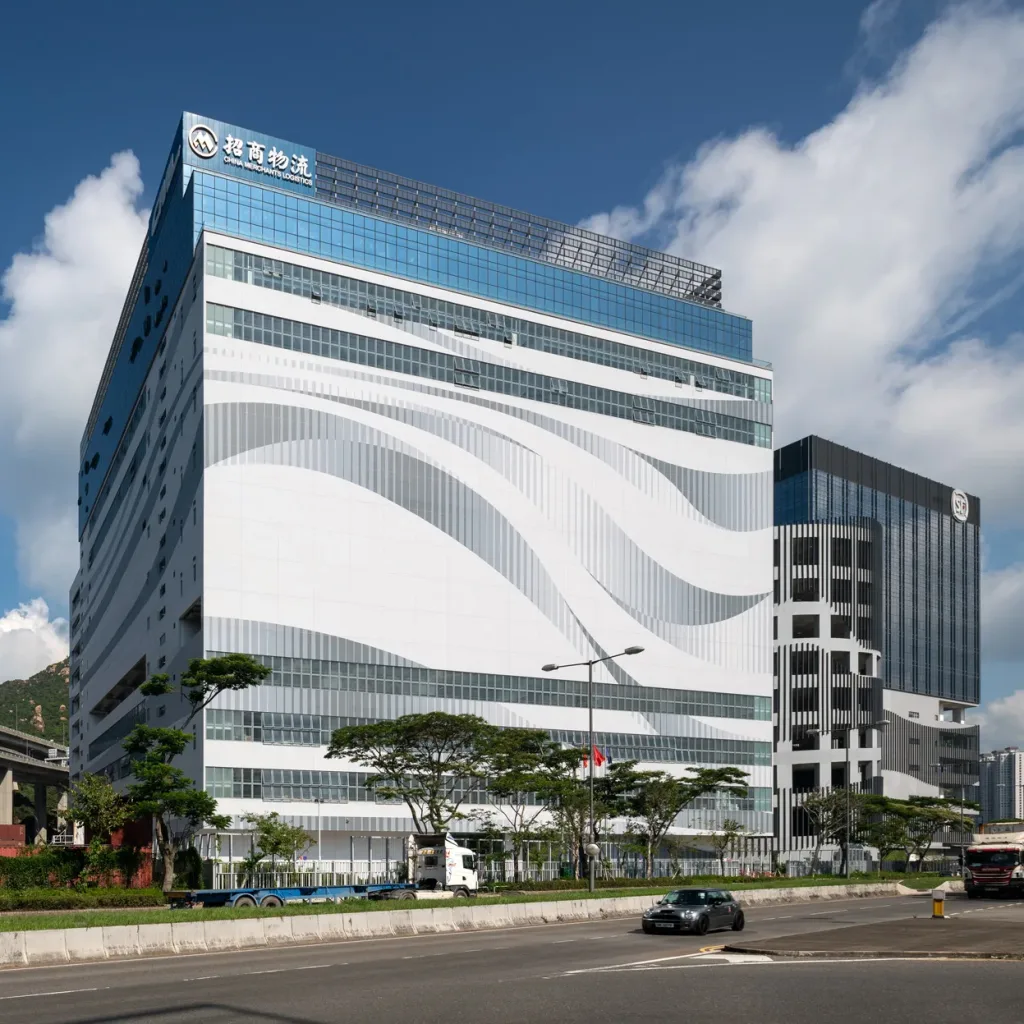 Aedas’ China Merchants Logistics Centre in Hong Kong is shown as a large‑scale logistics and office complex with a bold, wave‑patterned façade facing the waterfront. The image highlights a highly functional industrial building topped by cascading office terraces with extensive glazing, integrating efficient warehouse operations below with lighter, sea‑oriented office spaces above to create a distinctive logistics hub along the harbourfront.