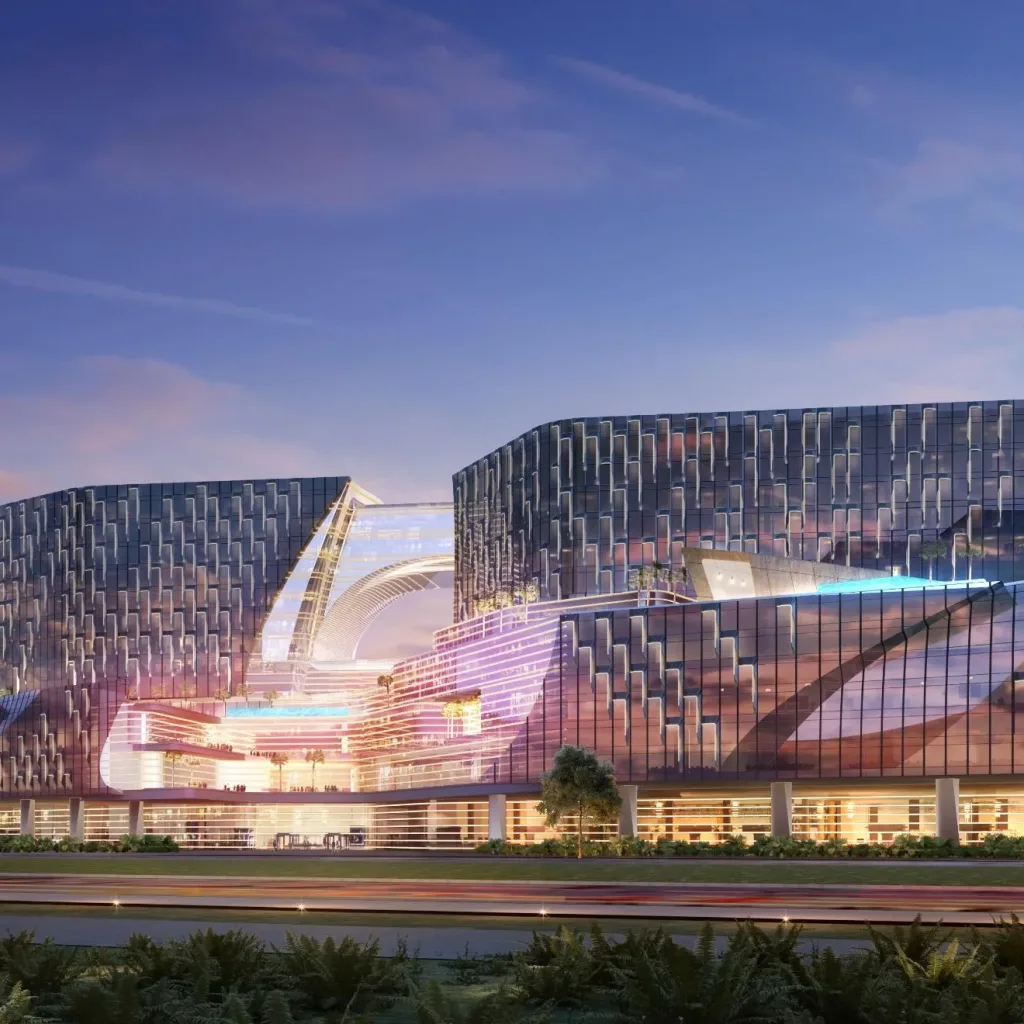 Aedas’s Westside City Integrated Resort in Manila is shown as a large‑scale resort complex with multiple sculpted building volumes, faceted glazed façades, and a continuous podium containing illuminated public spaces. The night‑time exterior highlights layered massing, expansive curtain walls, and destination‑scale hospitality architecture integrated within a landscaped coastal setting.