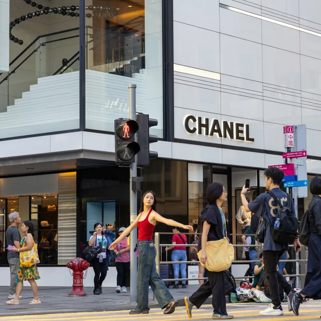 Aedas’ Centres of Central - luxury retail development in Hong Kong Central with double-height glazing façade, corner transparency and active street frontage. Street-level view of an Aedas-designed luxury retail building in Central, Hong Kong, featuring double-height high-performance glazing, aluminium panelled façade, recessed shopfront edges, and transparent corner conditions. The ground floor activates a pedestrian intersection with continuous glazing, integrated signage zones, and clearly defined urban thresholds.