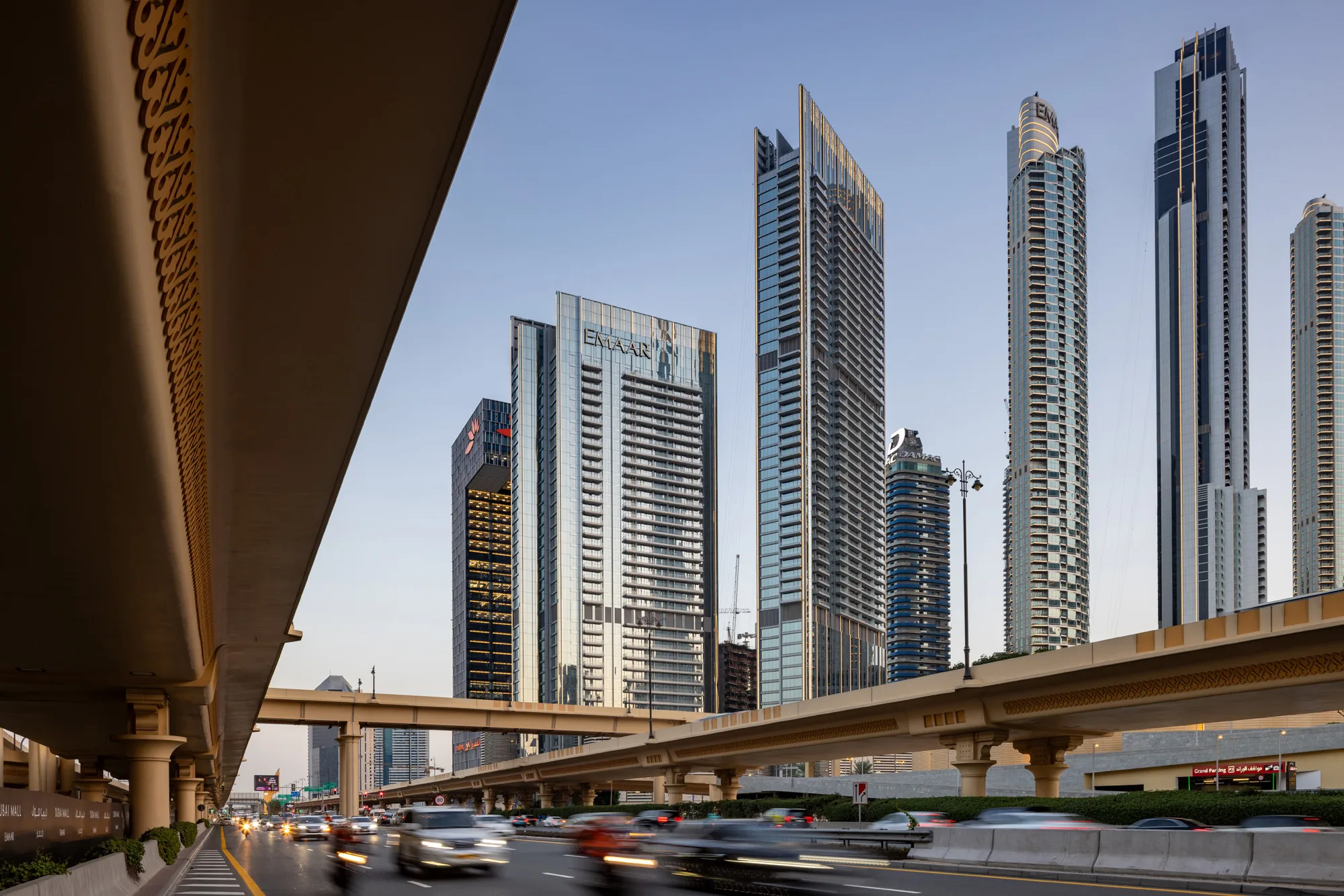 Aedas’ Vida Dubai Mall mixed-use towers with high-performance glazed façades and podium addressing a major Downtown Dubai boulevard. Street-level view of Aedas’ Vida Dubai Mall showing two slender high-rise towers with floor-to-ceiling curtain wall glazing rising from a shared podium. The development fronts a high-capacity urban boulevard and elevated road infrastructure, forming a distinct gateway condition within Downtown Dubai’s dense high-rise skyline.