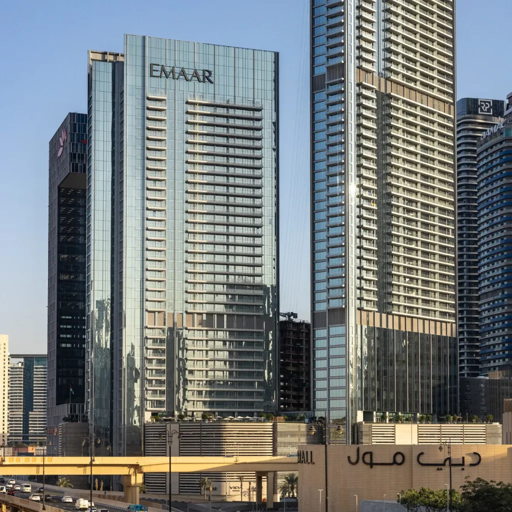 Aedas’ Vida Dubai Mall mixed-use towers with high-performance glazed façades and podium addressing a major Downtown Dubai boulevard. Street-level view of Aedas’ Vida Dubai Mall showing two slender high-rise towers with floor-to-ceiling curtain wall glazing rising from a shared podium. The development fronts a high-capacity urban boulevard and elevated road infrastructure, forming a distinct gateway condition within Downtown Dubai’s dense high-rise skyline.