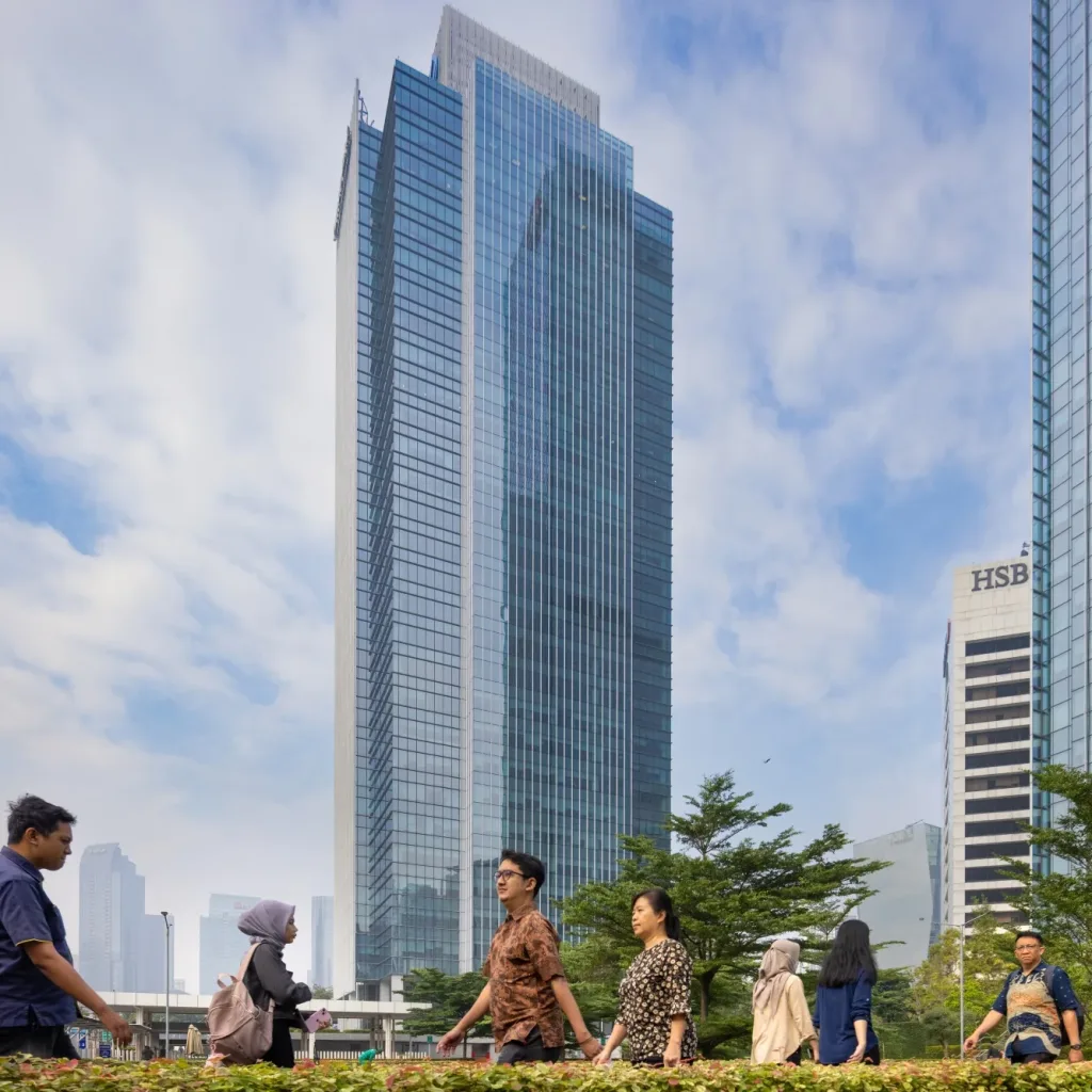 Aedas’ World Trade Center II & III in Jakarta with glass curtain walls, vertical fins and office towers along Jalan Sudirman. Street-level view of Aedas-designed World Trade Center II and III in Jakarta, showing high-rise office towers clad in glass curtain-wall façades with vertical and horizontal fins. The buildings rise from a shared urban podium along Jalan Jenderal Sudirman, with landscaped edges and pedestrian circulation in Jakarta’s central business district.
