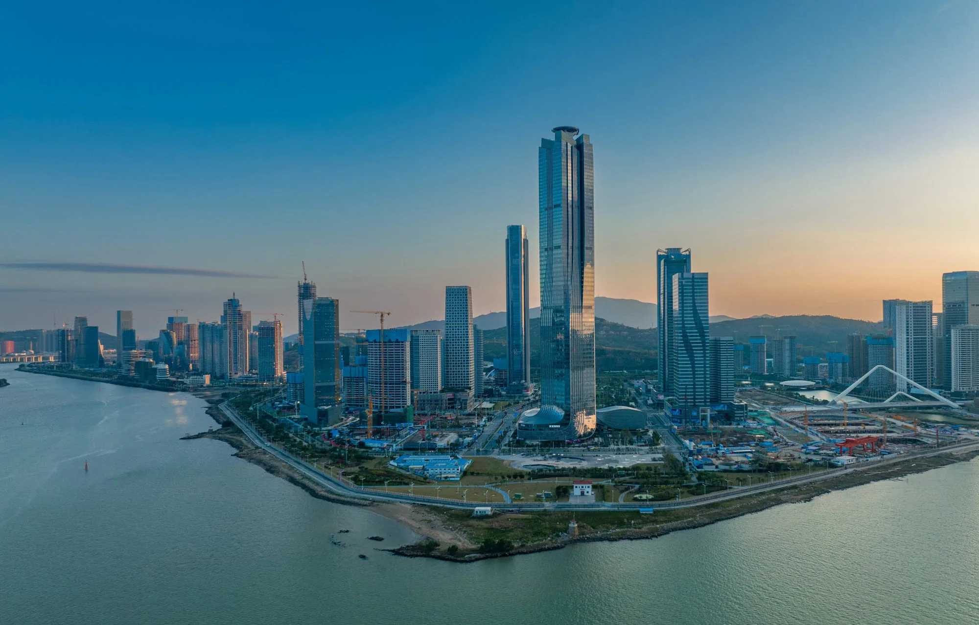 Aedas’s Zhuhai Shizimen CBD is depicted as a high‑density waterfront central business district with landmark high‑rise office towers, continuous podium development, and coastal public space. The image highlights integrated road infrastructure, reclaimed waterfront edges, and large‑scale CBD masterplanning positioned within the Hengqin development context.