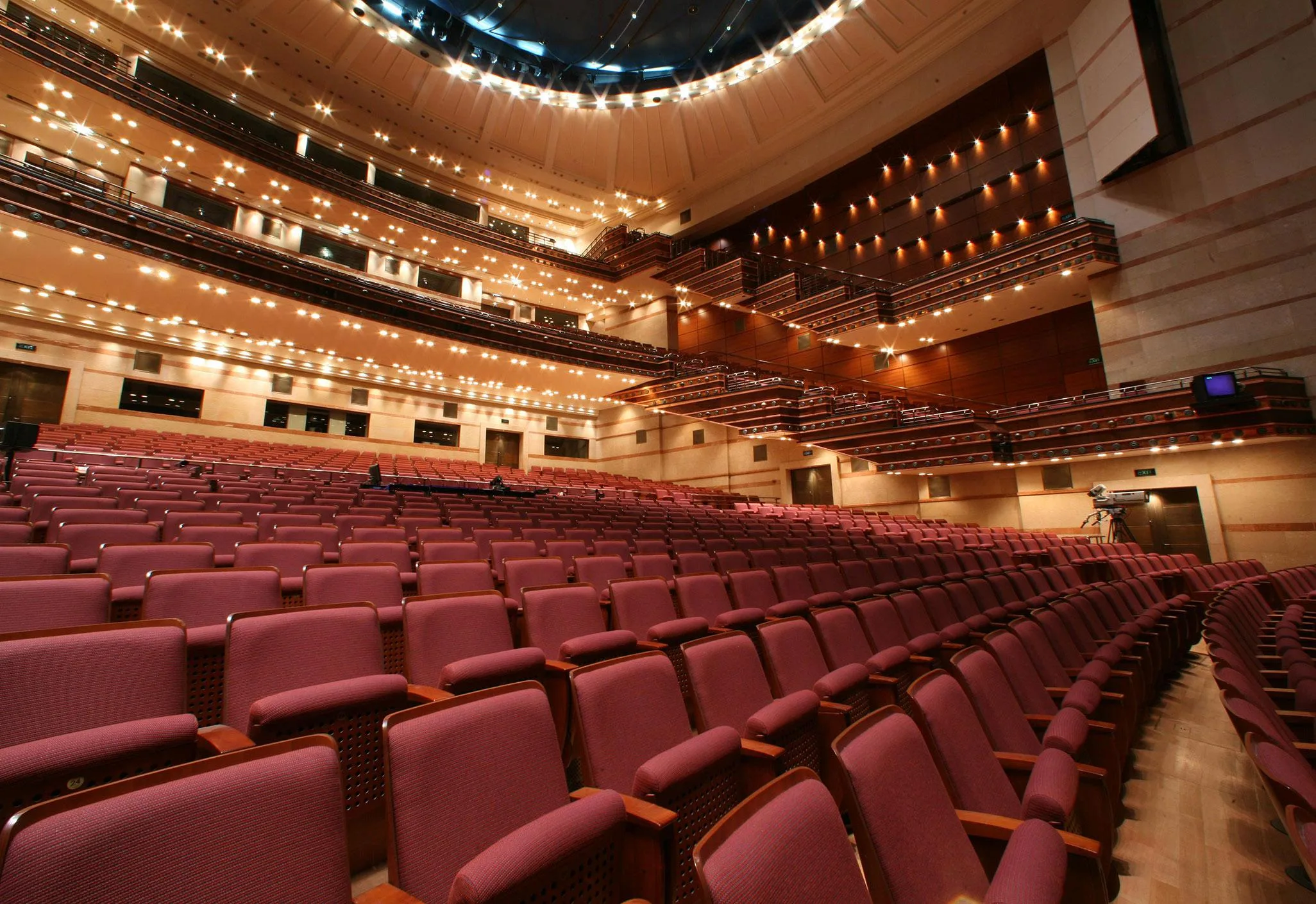 Aedas’s auditorium design at the AICC Megaron in Athens is shown with raked seating, multi‑level balconies, timber acoustic wall panels, and integrated ceiling lighting. The image highlights performance‑driven interior architecture, acoustic optimization, and large‑capacity cultural venue design within a Mediterranean urban context.