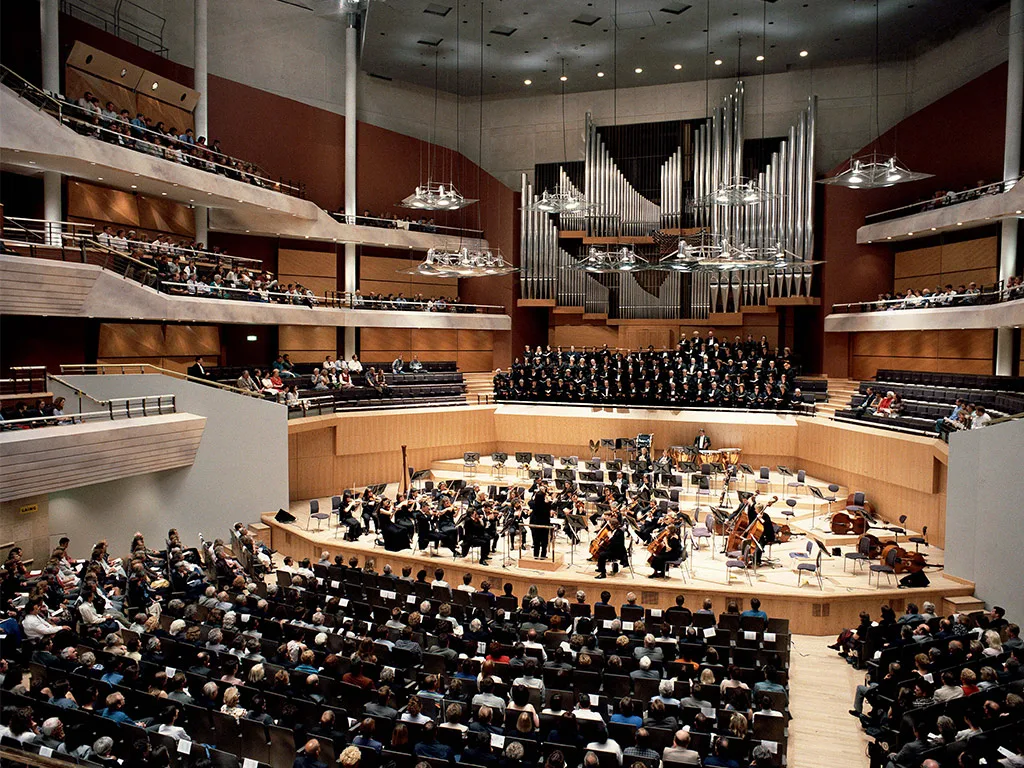 Aedas’s Bridgewater Hall in Manchester is shown as a purpose-built concert hall architecture with a terraced auditorium configuration, central performance platform, suspended acoustic reflectors, and a unified acoustic volume. The image demonstrates performance-led spatial geometry, large-capacity cultural infrastructure, and architectural integration of structure, acoustics, and circulation.