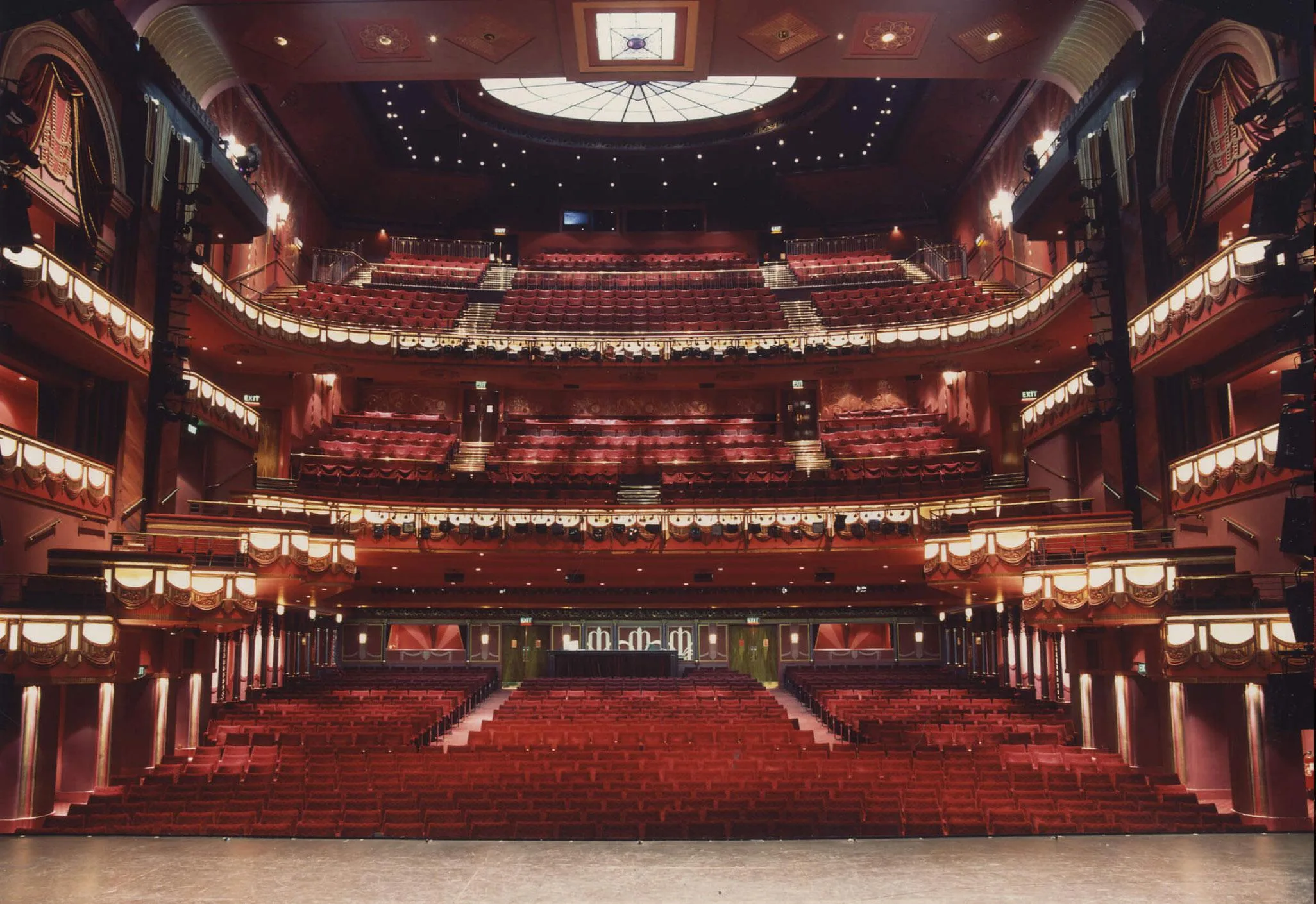 Aedas’s Prince Edward Theatre interior in London is shown with a multi‑tier auditorium, raked seating, ornate balcony fronts, and a framed proscenium stage. The image highlights heritage theatre architecture enhanced with integrated lighting, performance‑oriented sightlines, and acoustic envelope optimization suitable for large‑scale live productions.