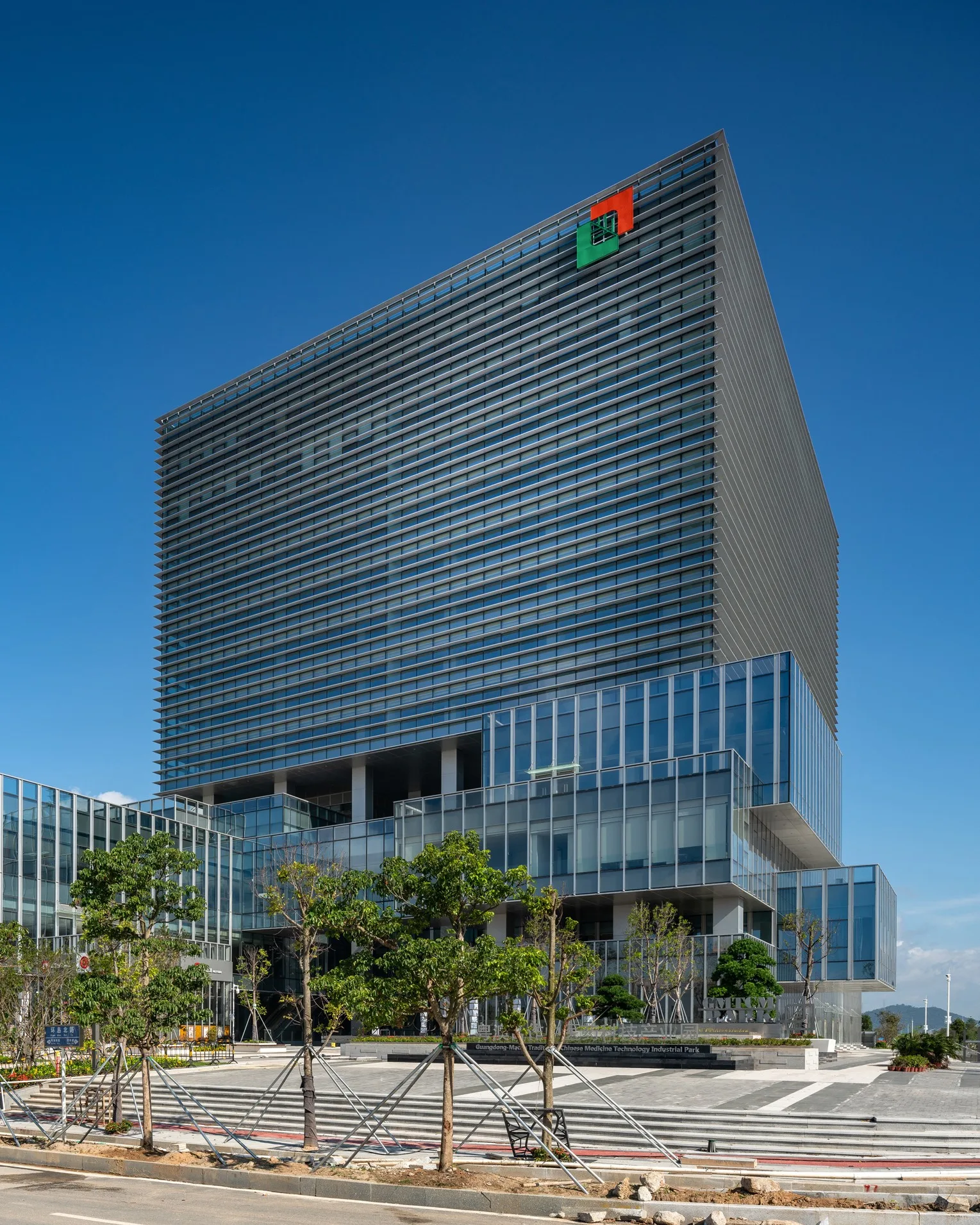 Aedas’s Headquarters for the Traditional Chinese Medicine Science and Technology Industrial Park in Zhuhai features interconnected towers with high-performance glazing, horizontal solar shading, and landscaped permeable paving. The subtropical climate context informs passive cooling strategies, net-zero energy design, and biophilic integration, reinforcing adaptive reuse potential and Passive House standards.