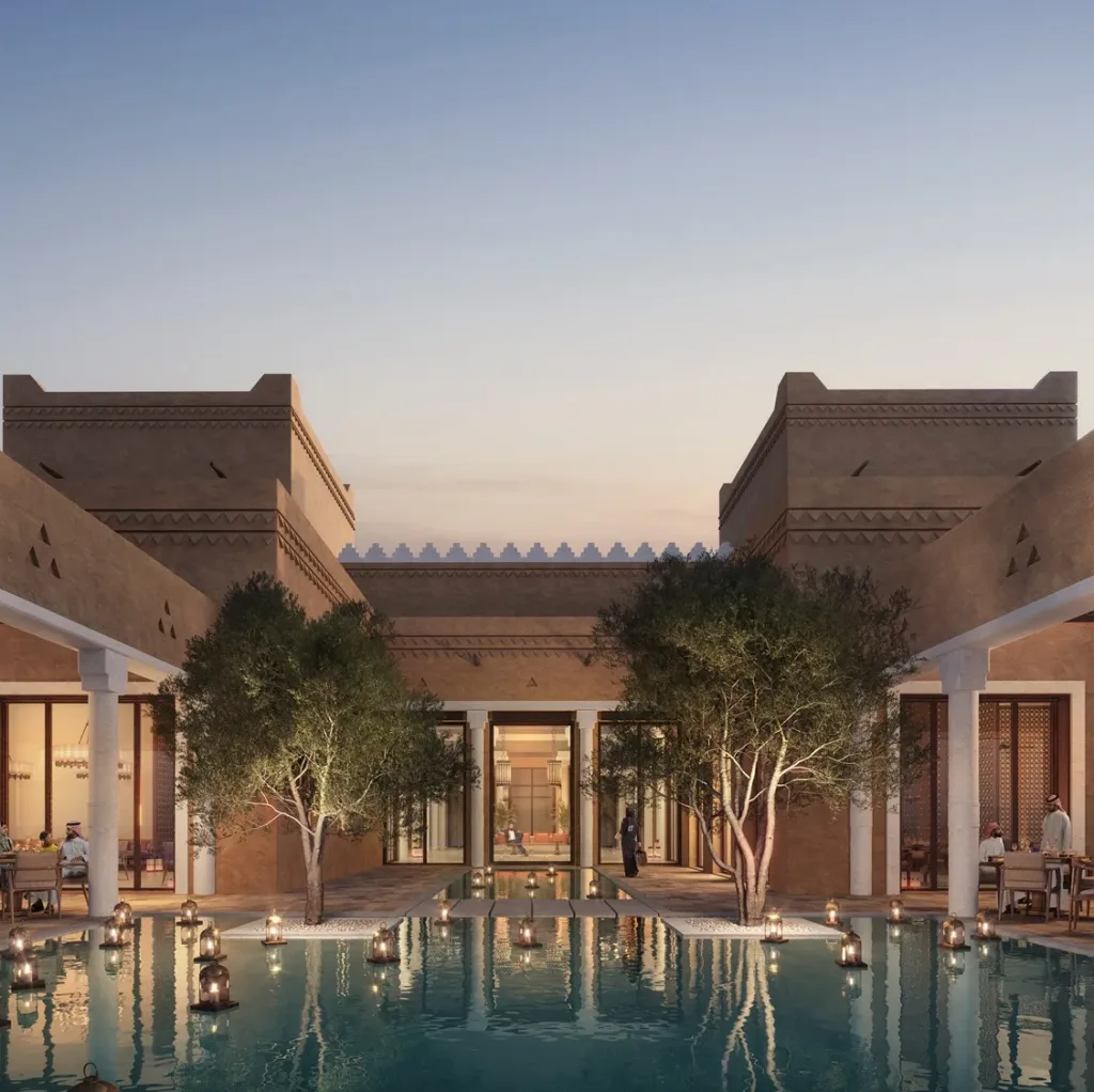 Aedas’ The Oberoi Wadi Safar—low-rise luxury resort with courtyard villas, palm groves and central water axis in desert terrain. Aerial dusk view of Aedas’ The Oberoi Wadi Safar in Saudi Arabia: low-rise resort villas organised along a linear water axis, framed by palm groves and courtyards. Earth-toned masonry volumes sit within desert topography, forming shaded pedestrian paths. Visible planning supports courtyard-based passive cooling, climate-responsive resort design and landscape-integrated luxury hospitality.